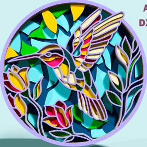 May include: A layered paper art piece featuring a hummingbird in flight, surrounded by flowers and foliage. The design incorporates vibrant colors like yellow, pink, and blue, set within a circular frame. Text on the right side reads "SVG AI DXF".