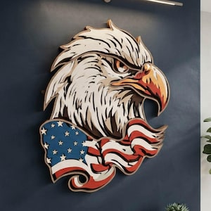 May include: A layered wall art piece featuring a stylized eagle head with a sharp, orange-toned beak, positioned above a flowing American flag design with blue, white, and red colors. The text DXF AI SVG DIGITAL FILE FOR LASER CUT is visible.