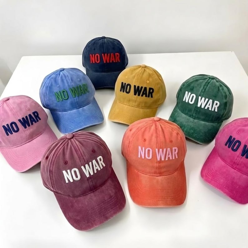 May include: A collection of eight baseball caps in various colors, including pink, blue, and yellow. Each cap features the embroidered text "NO WAR" in a contrasting color. The caps are arranged on a white surface.