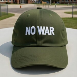 May include: Olive green baseball cap with the white embroidered text "NO WAR" across the front. The cap has a curved brim and a button on top. The background shows a schoolyard.