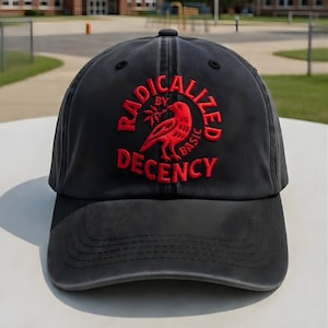 May include: Black baseball cap with the embroidered text "RADICALIZED BY BASIC DECENCY" in red. The design includes a red bird holding a branch. The cap has a curved brim and a fabric strap closure.