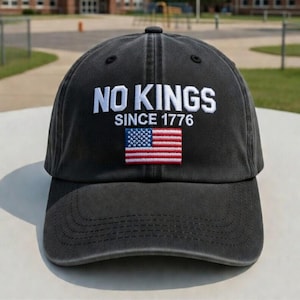 May include: A black baseball cap with the text "NO KINGS SINCE 1776" embroidered in white above a small American flag patch. The cap has a curved brim and a rounded crown.