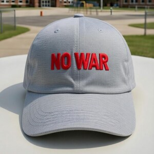 May include: A light gray baseball cap with the embroidered text "NO WAR" in red. The cap has a curved brim and a fabric texture. The hat is sitting on a white surface.