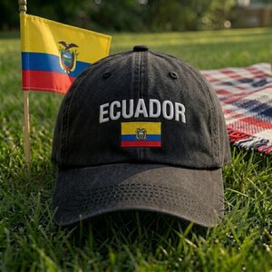 May include: A black baseball cap featuring the word ECUADOR embroidered in white capital letters above a small, rectangular patch of the Ecuadorian flag, which consists of horizontal yellow, blue, and red stripes with a central coat of arms.