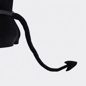 May include: A black plush tail accessory featuring a long, flexible design with a pointed, spade-shaped tip. The tail is attached to a simple black belt, crafted from a soft, velvety fabric that maintains a curved shape extending outward.