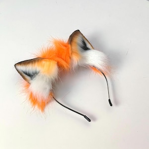 Op de afbeelding: Een haarband met vossenoren. De oren zijn gemaakt van oranje, witte en bruine imitatiebont. De haarband is zwart en heeft een eenvoudig ontwerp. Een leuk accessoire.