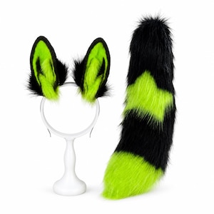 May include: A set of faux fur animal ears attached to a headband and a matching long faux fur tail. The ears and tail feature a vibrant neon green and black striped pattern, with black fur trim along the edges of the pointed ear shapes.