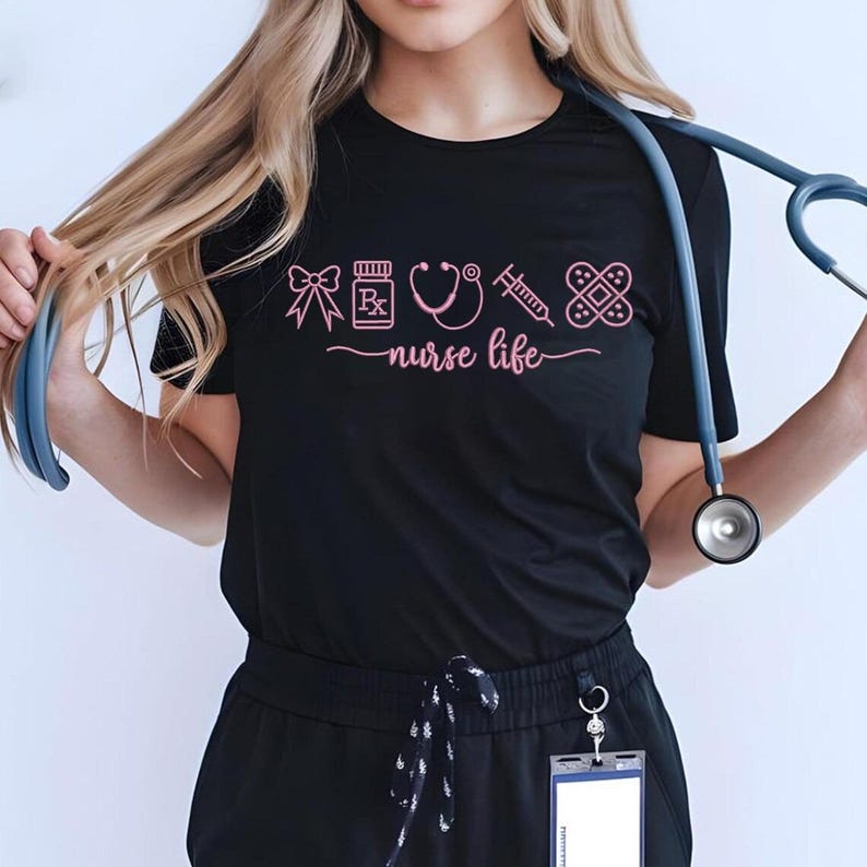May include: Black t-shirt with pink graphic icons of medical supplies and the words "nurse life". A stethoscope hangs around the neck. The shirt is made of a soft material.