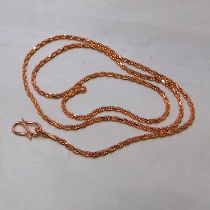 Pode incluir: Um colar em tom de ouro rosa com um design de corrente de corda torcida. O colar apresenta um fecho de gancho. A corrente é exibida em uma superfície de cor clara.