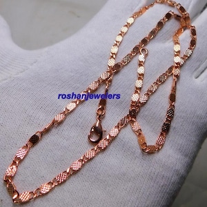 Peut inclure: Un collier en chaîne de couleur or rose composé d'une série de maillons ovales texturés et interconnectés avec un motif quadrillé. Le collier comprend un fermoir mousqueton et affiche le texte bleu roshanjewelers imprimé sur la surface.