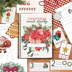 Op de afbeelding: Een educatieve set met kerstthema, met een spiraalgebonden boek getiteld "Christmas Unit Study", samen met flashcards, een peperkoekboom en een elf-illustratie. De items zijn gerangschikt op een houten oppervlak.
