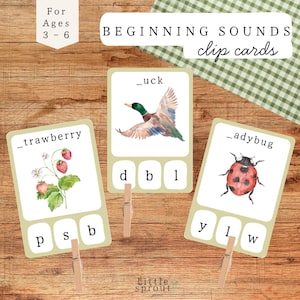 Puede incluir: Tarjetas de pinza educativas para niños de 3 a 6 años con ilustraciones de una fresa, un pato y una mariquita. Las tarjetas están diseñadas para enseñar los sonidos iniciales. El texto en las tarjetas dice "Beginning Sounds clip cards".