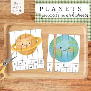 May include: A wooden tray holds two planet-themed puzzle worksheets, one depicting Saturn and the other Earth. The worksheets are divided into numbered sections for ages 3-6. The text "PLANETS puzzle worksheets" is visible.