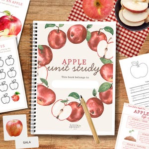 May include: A spiral-bound notebook with the title "APPLE unit study" and a watercolour apple design. The cover features the text "This book belongs to" and is surrounded by illustrations of red apples and green leaves. A pencil rests on the cover.