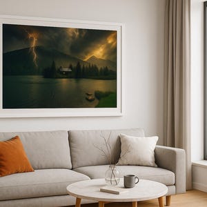 May include: A framed landscape print depicts a cabin on a small island in a lake, with a dramatic sky illuminated by lightning. The artwork is displayed above a gray sofa with orange and white pillows. A round coffee table and a window with a view of the Eiffel Tower complete the scene.
