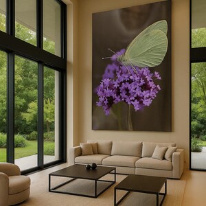 May include: A large canvas print of a butterfly on purple flowers hangs above a beige sofa. The butterfly is pale green, and the flowers are a vibrant purple. The room has large windows and a neutral color palette.