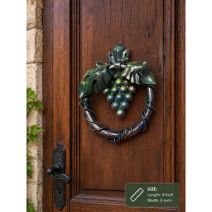 May include: A metal door knocker with a grape cluster design. The knocker has a silver finish with green detailing. It measures approximately 20 cm in length and 15 cm in width.
