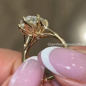 Op de afbeelding: Een gouden ring met een grote, ronde, gefacetteerde heldere edelsteen in een zeskantige zetting die lijkt op een bloemknop. De ringband is van gepolijst goud en de tekst GlamPearlsJewelsShop is zichtbaar aan de zijkant van de zetting.