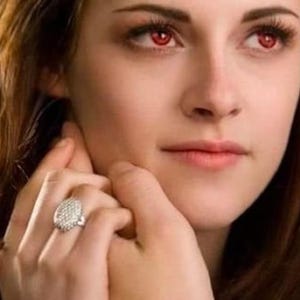 Puede incluir: Primer plano de una persona con ojos rojos y piel clara. La persona lleva un anillo con una piedra grande y redonda con forma de diamante. La persona tiene el pelo largo y castaño y mira al espectador.