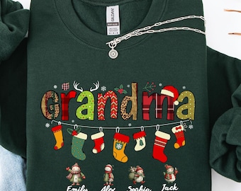 May include: A dark green sweatshirt with the word "grandma" in a festive design, featuring Christmas stockings and the names Emily, Alex, Sophia, and Jack. A silver necklace with a pendant is also visible.
