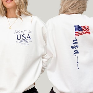 Puede incluir: Sudadera blanca con el texto "Faith & Freedom USA" y la fecha 1776. La parte trasera presenta una inscripci&oacute;n vertical "usa" y una bandera americana. El dise&ntilde;o es en azul marino.