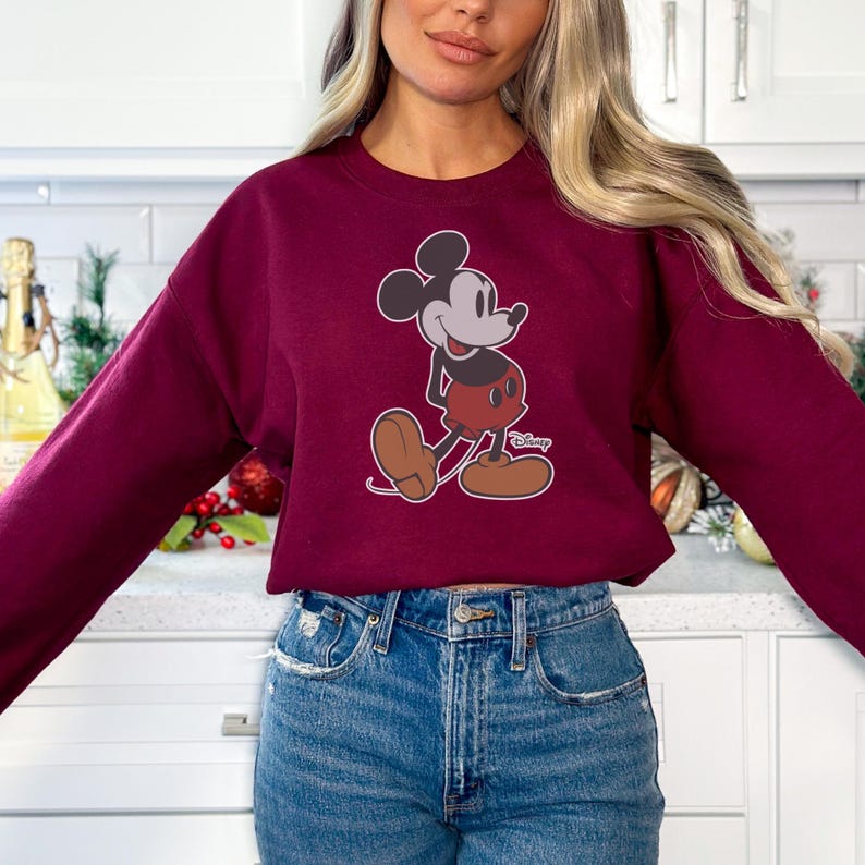 K&ouml;nnte beinhalten: Burgunderfarbenes Sweatshirt mit einem Mickey Mouse-Motiv. Die Zeichentrickfigur ist in ihrer klassischen Pose dargestellt und tr&auml;gt rote Shorts und braune Schuhe. Das Sweatshirt ist einfarbig burgunderfarben und hat lange &Auml;rmel.