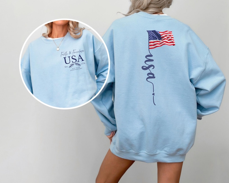 Puede incluir: Sudadera azul claro con la palabra "USA" y "Faith & Freedom" estampadas en la parte delantera. La parte trasera presenta una inscripci&oacute;n vertical "usa" y una bandera americana. La sudadera es de cuello redondo.