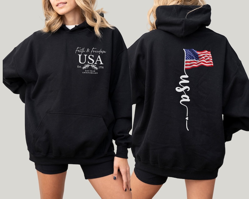 Puede incluir: Sudadera con capucha negra con bolsillo delantero y capucha. La parte delantera presenta el texto "Faith & Freedom USA" con un emblema y "Est. 1776 200 Year Anniversary". La parte trasera muestra una bandera americana ondeando y la palabra "usa" en cursiva.