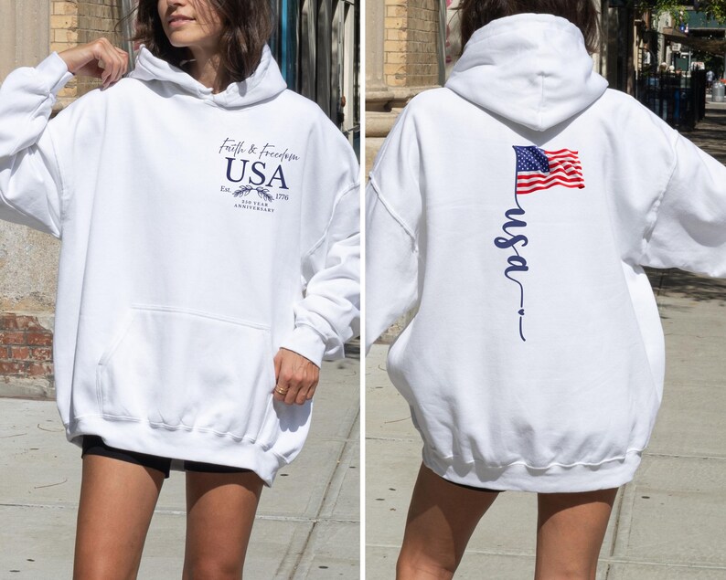 Puede incluir: Sudadera con capucha blanca con bolsillo delantero y el texto "Faith & Freedom USA" con un emblema. La parte trasera presenta una bandera estadounidense ondeando y la palabra "usa" en escritura cursiva. Una prenda casual y patri&oacute;tica.