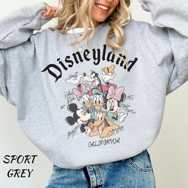 May include: Sport grey sweatshirt featuring the word "Disneyland" in a black script font. The sweatshirt has a graphic of Disney characters including Mickey Mouse, Minnie Mouse, Donald Duck, and Goofy. The word "California" is printed at the bottom.