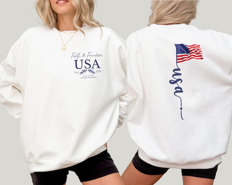 Puede incluir: Sudadera blanca con el texto "Faith & Freedom USA" y la fecha 1776. La parte trasera presenta una inscripci&oacute;n vertical "usa" y una bandera americana. El dise&ntilde;o es en azul marino.