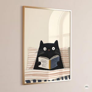 May include: A framed art print featuring a black cat reading a book in bed. The cat has large, wide eyes and is nestled under a striped blanket and pillow. The frame is gold-colored.