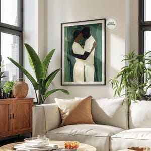 May include: A framed art print depicts a couple embracing, rendered in a minimalist style. The figures are in white and black against a green background. The artwork is displayed in a modern living room setting with a neutral-toned sofa and plants.