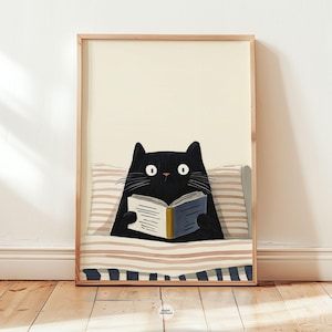 May include: A framed art print featuring a black cat reading a book in bed. The cat has large white eyes and is surrounded by a striped pillow and blanket. The frame is a light brown color, and the background is a cream color.