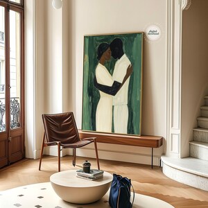 May include: An abstract painting depicts two figures embracing, set against a green backdrop. The figures are rendered in black and white, with the couple's arms wrapped around each other. The artwork is framed in gold and hangs above a wooden bench.