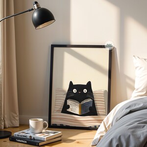 May include: A framed art print featuring a black cat reading a book, resting on a striped pillow. A black floor lamp with a white interior shade is positioned to the left. A white mug sits atop a stack of books.