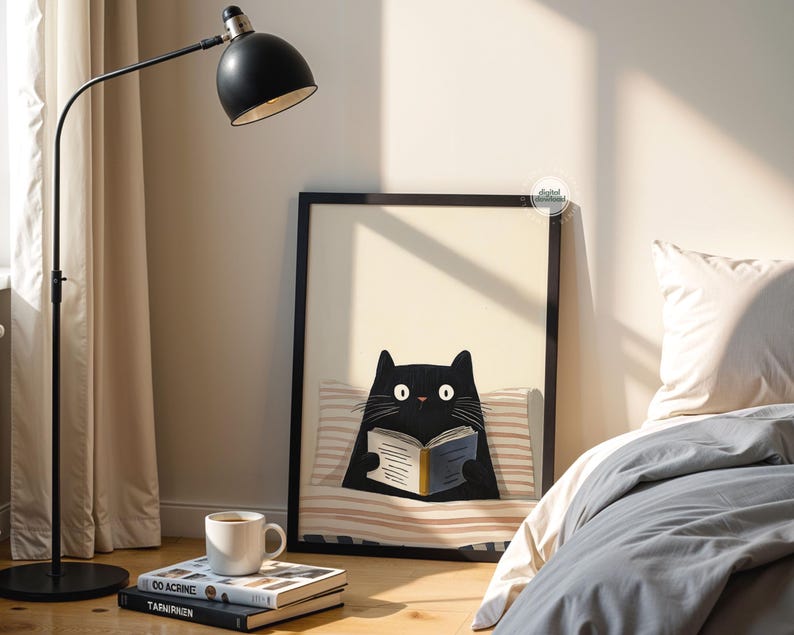 May include: A framed art print featuring a black cat reading a book, resting on a striped pillow. A black floor lamp with a white interior shade is positioned to the left. A white mug sits atop a stack of books.