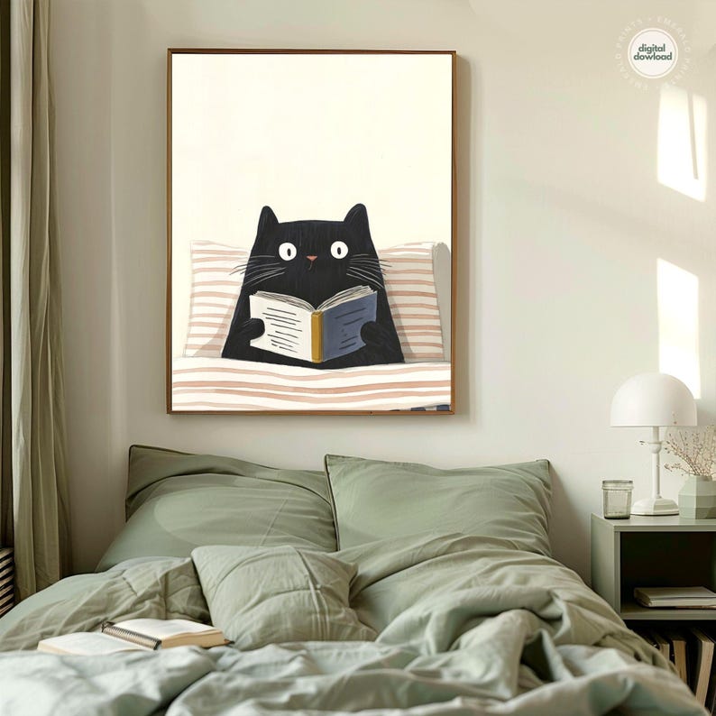 May include: A framed art print featuring a black cat reading a book. The cat is depicted with large white eyes and is resting on a striped pillow. The book has a blue cover and yellow spine. The artwork is displayed on a white wall.