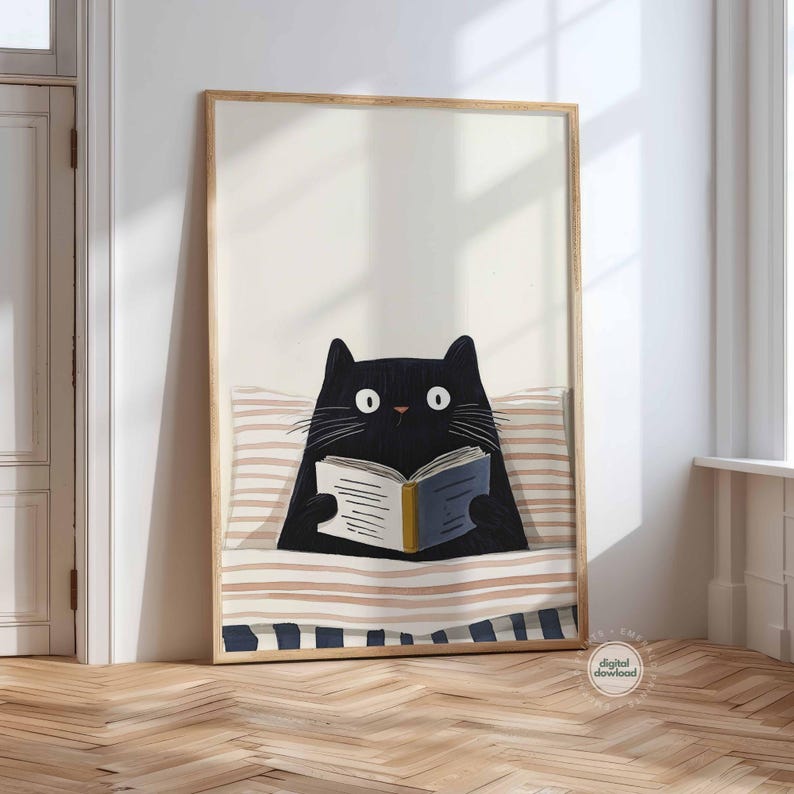 May include: A framed art print featuring a black cat reading a book in bed. The cat has large white eyes and is nestled under a striped blanket. The book has blue and yellow accents. The frame is a light wood color.