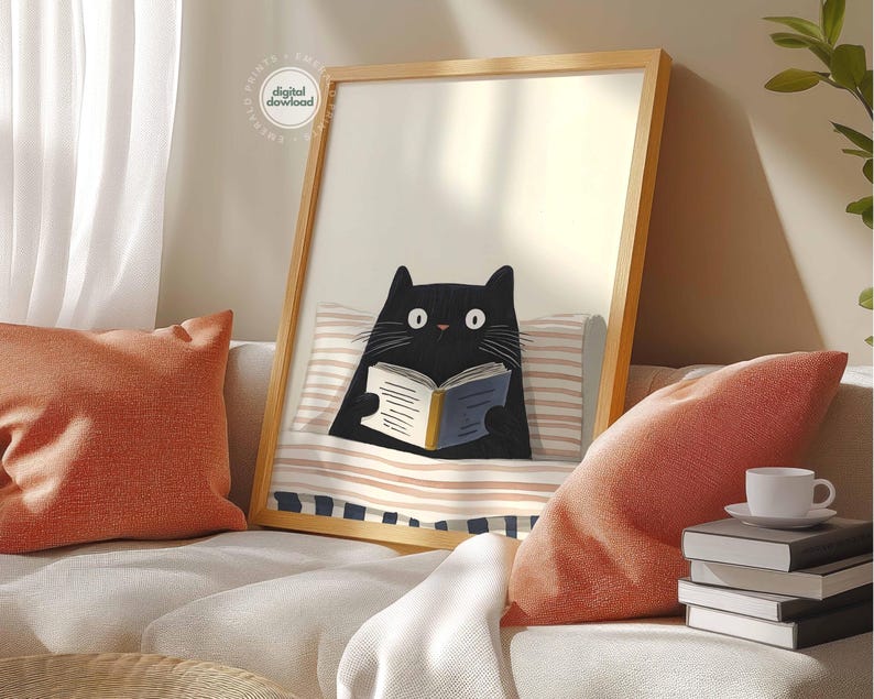 May include: A framed art print featuring a black cat reading a book while lying in bed. The cat has wide eyes and is holding a book with a blue cover. The print is in a wooden frame and is displayed on a sofa with orange pillows.