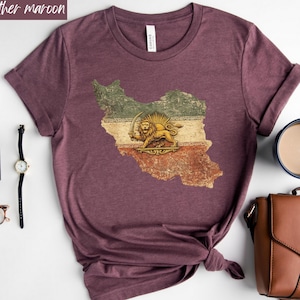 May include: Heather maroon t-shirt featuring a distressed graphic of the Iranian flag in the shape of the country. The flag design includes a lion holding a sword. The shirt is a crew neck style.