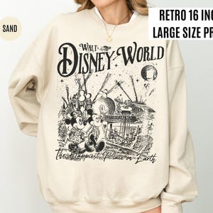 Peut inclure: Sweat-shirt couleur sable avec un motif noir et blanc de Walt Disney World, Mickey et Minnie Mouse, et le texte "The Happiest Place on Earth". Le sweat-shirt a un col rond et des manches longues. Le texte "Retro 16 inch Large Size Print" est &eacute;galement visible.
