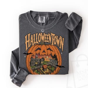 May include: A charcoal gray long-sleeve sweatshirt featuring a large orange jack-o'-lantern graphic with the text HALLOWEENTOWN. Inside the pumpkin is a detailed illustration of a town square with buildings, a smaller pumpkin, and bats.