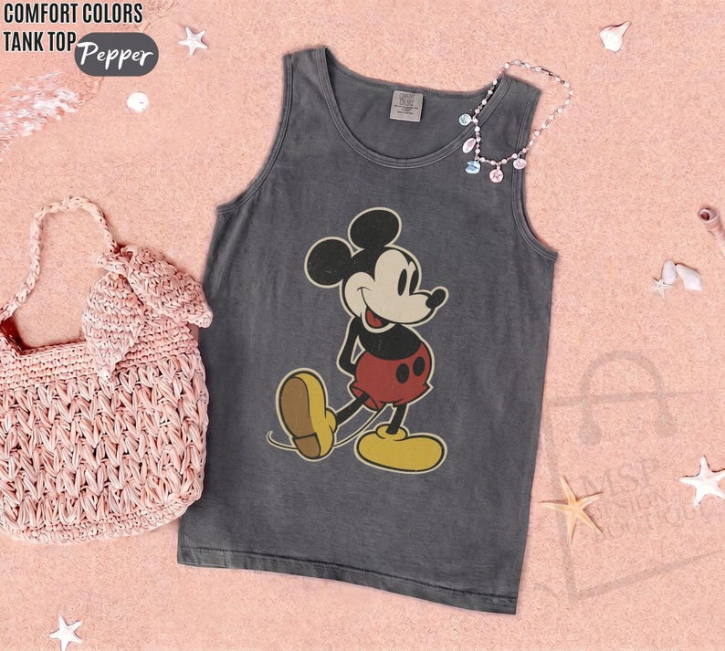 May include: Gray tank top featuring a classic Mickey Mouse graphic. The sleeveless shirt has a vintage look, with a distressed appearance. The image also includes a pink woven handbag and a necklace with colorful beads. The words "COMFORT COLORS TANK TOP Pepper" are in the top left corner.