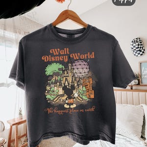 May include: Dark gray boxy tee with a Walt Disney World graphic. The design features a castle, Spaceship Earth, and Mickey Mouse. Text includes "Walt Disney World" and "The happiest place on earth". The shirt is labeled "Comfort Colors - Boxy Tee" and the color is "Pepper".
