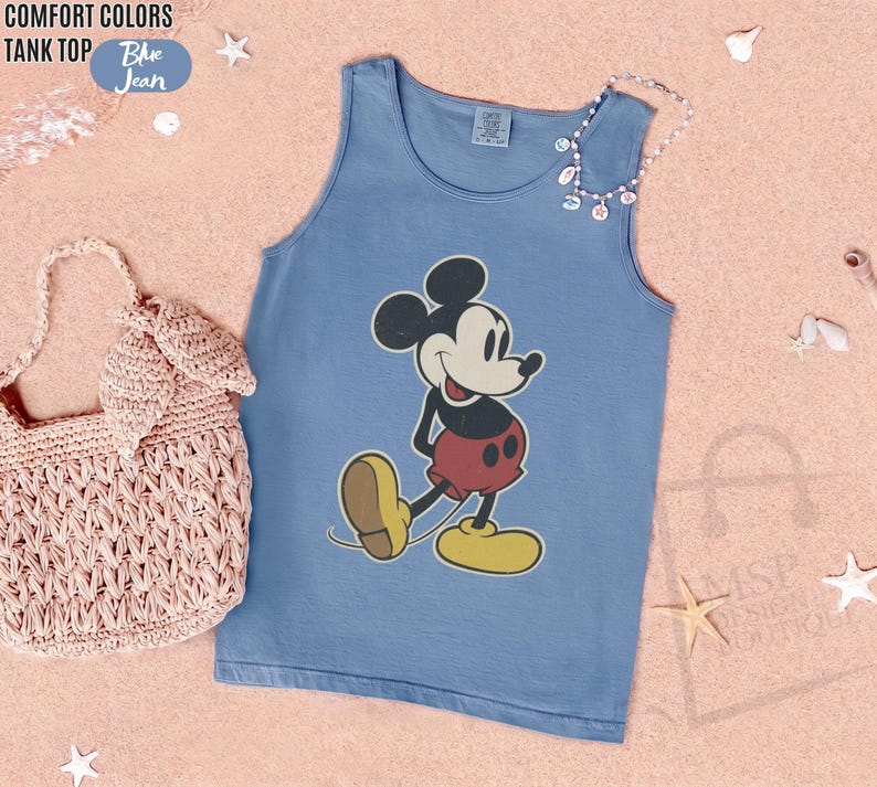 May include: A blue tank top featuring a classic Mickey Mouse graphic. The sleeveless shirt has a round neckline and is made of a soft material. The words "COMFORT COLORS" and "TANK TOP" are printed on the top left of the image, and the word "Blue Jean" is printed on a blue oval.