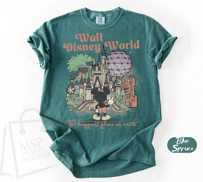 May include: Teal-colored t-shirt featuring a graphic of Walt Disney World with Mickey Mouse. The design includes the text "Walt Disney World" and "The happiest place in earth". The shirt has a crew neck and short sleeves.