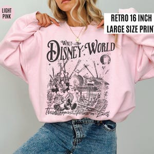 Peut inclure: Sweat-shirt rose clair avec un motif noir et blanc de Walt Disney World. Le motif comprend Mickey et Minnie Mouse, le texte "Walt Disney World" et "The Happiest Place on Earth". Le sweat-shirt porte l'inscription "Retro 16 inch Large Size Print".