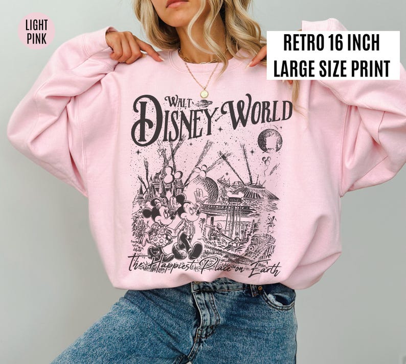 Peut inclure: Sweat-shirt rose clair avec un motif noir et blanc de Walt Disney World. Le motif comprend Mickey et Minnie Mouse, le texte "Walt Disney World" et "The Happiest Place on Earth". Le sweat-shirt porte l'inscription "Retro 16 inch Large Size Print".