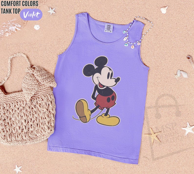 May include: Violet tank top featuring a classic Mickey Mouse graphic. The tank top is a light purple color and has a round neckline. The words "COMFORT COLORS TANK TOP" and the color "Violet" are printed on the top left corner.